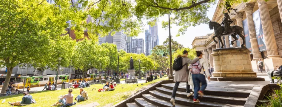 Two people going up State Library Victoria entrance stairs and statue